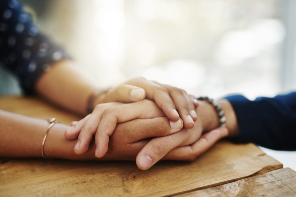 Holding hands, support and closeup with trust, solidarity and community on a home table.